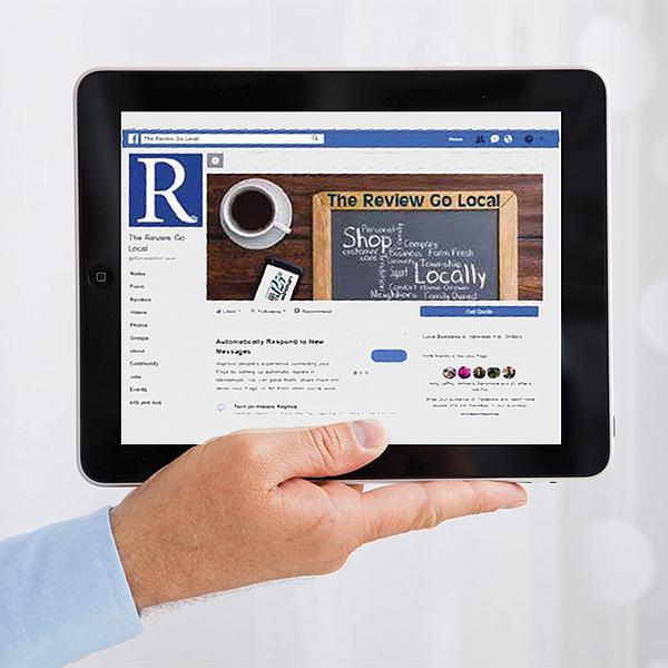A hand holding a tablet that is showing The Review Facebook page which is a great place to have a Facebook Advertising Post Package.